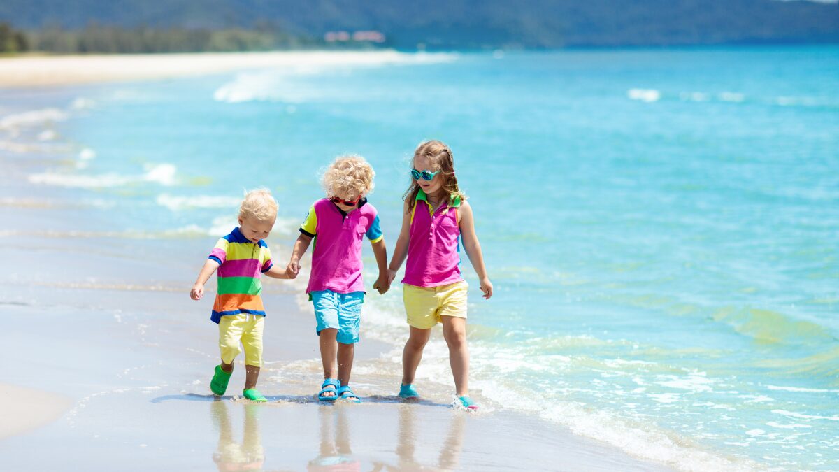 カラフルな服を着た兄弟が綺麗な浜辺を歩いている様子